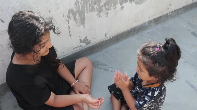 Two Indian sisters sitting together outdoors, sharing a playful and affectionate moment in a residential setting.