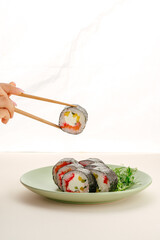 Woman holding a fresh sushi roll with chopsticks © Cavan