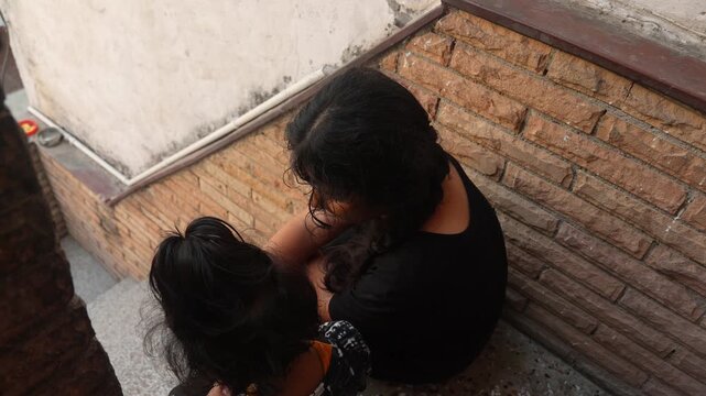 Top view of an Indian mother and child sitting together on a narrow rooftop staircase, sharing a quiet moment at home.