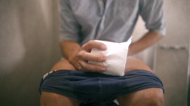 Person Sitting On Toilet Holding Stomach Suffering From Abdominal Pain In Bathroom 