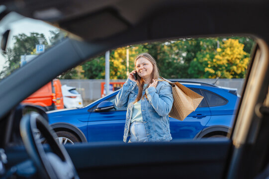 Smiling woman with shopping bag talks on phone in parking lot