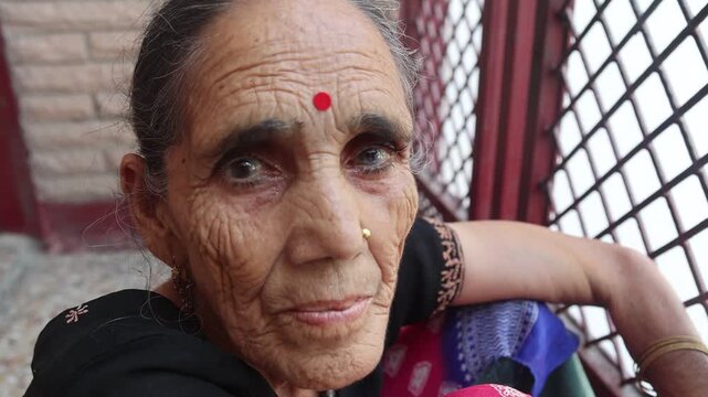 Close-up portrait of an elderly Indian woman wearing a red bindi and traditional clothing, looking at the camera with a natural and expressive facial expression.