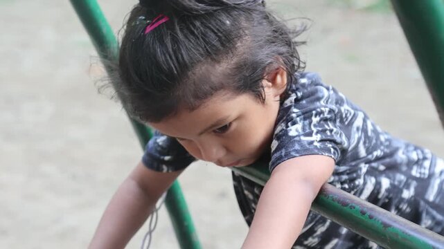 Indian girl sitting on playground equipment, looking down and appearing thoughtful or lost in thought.
Candid childhood moment showing a quiet and thoughtful child enjoying time outdoors.