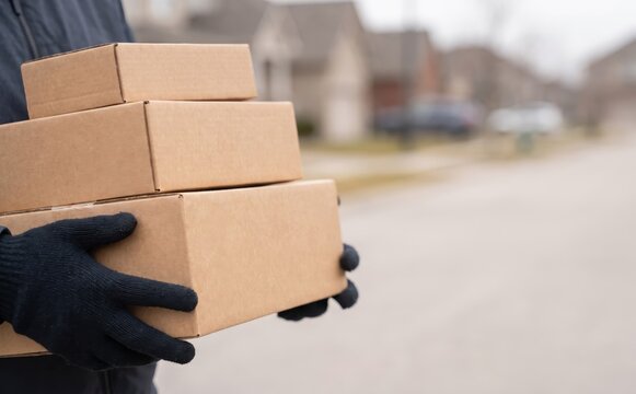 Delivery person holding a stack of cardboard packages for shipment in a residential neighborhood concept of courier services and online shopping