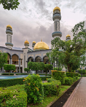 The beautiful Jame' Asr Hassanil Bolkiah Mosque with its golden domes and minarets in a lush garden setting, located in Bandar Seri Begawan, Brunei under a dramatic cloudy sky