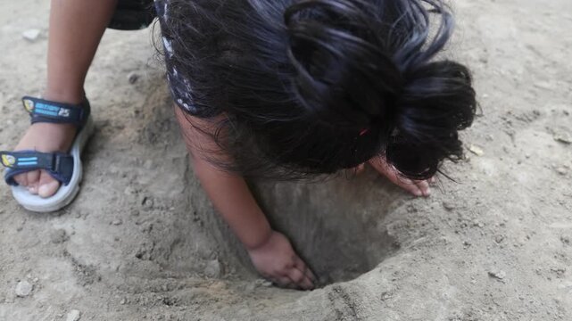 Indian child investigating a small hole in dry soil while playing outdoors, reaching into the earth with curiosity and concentration, capturing authentic rural childhood, exploration, and traditional 