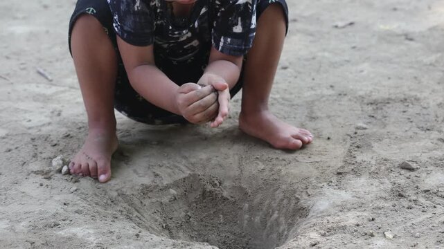 Indian village girl sitting barefoot near a small pit and playing with soil, enjoying a simple childhood activity in a rural outdoor environment.