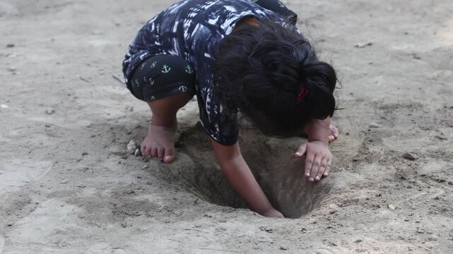 Young Indian child playing outdoors in the dirt, digging into the soil with her hands and enjoying a fun, natural childhood activity.
