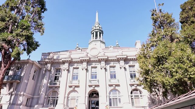 Camera shot of the historic Old City Hall in Berkeley, California, showing its beautiful Beaux-Arts architecture with a central clock tower and tall green trees framing the building