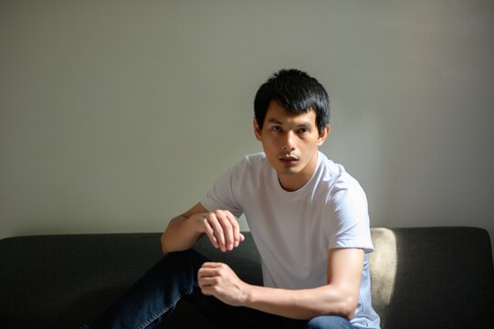 Young Man in Casual White Shirt Posing on Sofa in Natural Light
