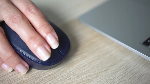 A young woman uses a computer mouse while working on a laptop.