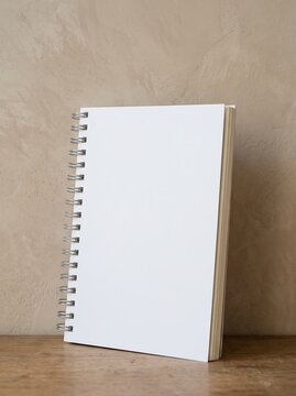 Blank white cover wire bound spiral notebook standing upright against textured limewash plaster wall