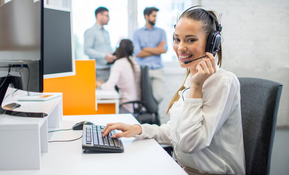 Smiling young businesswoman with headset looking at camera in call center