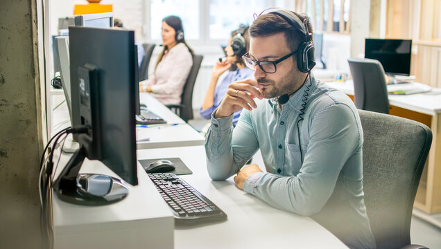 Thoughtful young man customer support agent with headset working at desk