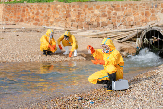 Team of scientists in hazmat suits collecting water sample from drainage pipe stream, Environmental researchers testing wastewater at river outlet, Specialists investigating toxic water pollution