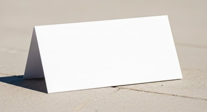 Blank white folded card standing on a textured concrete surface, perfect for mockups and graphic design.