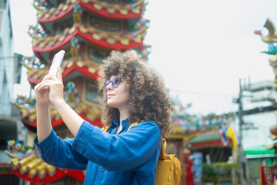 Caucasian woman travel vlogger photographing colorful Chinese shrine with smartphone in Thailand