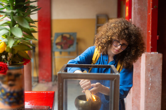 Caucasian woman traveler lighting incense sticks at Asian temple during cultural sightseeing trip