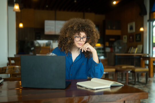 Caucasian Woman with Curly Hair Working on Laptop in Cozy Cafe Coffee Shop