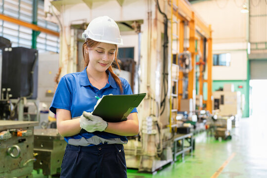 Female worker writing on clipboard in industrial manufacturing plant, Smiling engineer holding clipboard and inspecting workshop production, Technician checking inventory on clipboard in factory