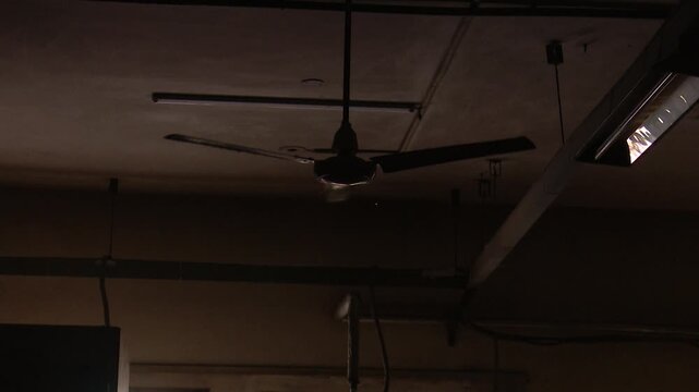 Garment factory experiencing power outage with ceiling fans spinning but no lights during manufacturing work