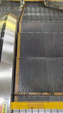 Moving Escalator Steps Downward View. Continuous motion of metallic escalator stairs descending, showing grooved steps, side railing, and yellow safety edge line in modern indoor space. 4k 60fps video