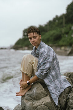 Pensive woman sitting barefoot on a rocky shore