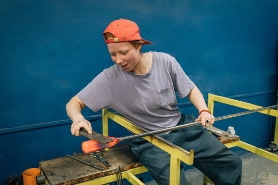 Young glassblower shapes molten glass in workshop