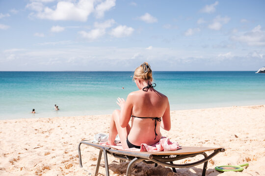 Woman in bikini applying sunscreen on a beach lounger