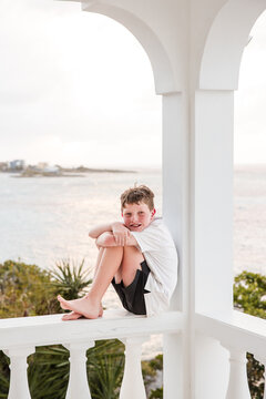 Happy boy sits barefoot on a seaside balcony