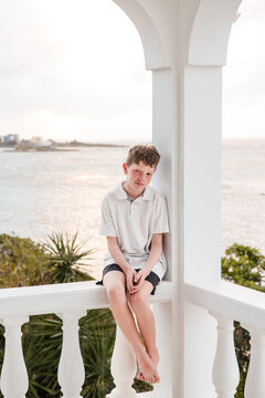 Young boy with freckles sitting on a white balcony by the sea