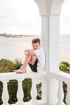 Young boy sitting on a white balcony overlooking the ocean