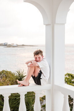 Young boy smiles on a white balcony overlooking the ocean