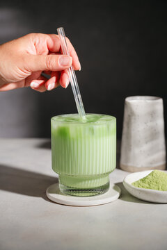Womans hand stirring a refreshing iced matcha latte