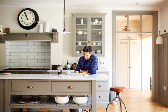 Morning, breakfast and man with tablet in kitchen, smile and reading ebook on website or literature. Happy, reader and person with food, fiction and entertainment with technology and novel in home