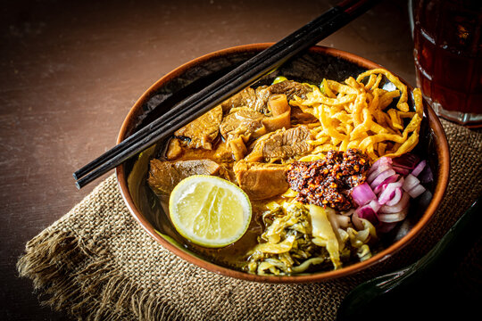 Northern Thai pork khao soi with crispy noodles, fresh lime, red onions, and pickled mustard greens, perfectly paired with a refreshing iced butterfly pea tea.