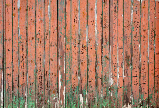 Weathered wooden weatherboarding in Lavenham, Suffolk, with faded orange paint peeling to reveal green undercoat, showing the rustic character of this historic English wool town.