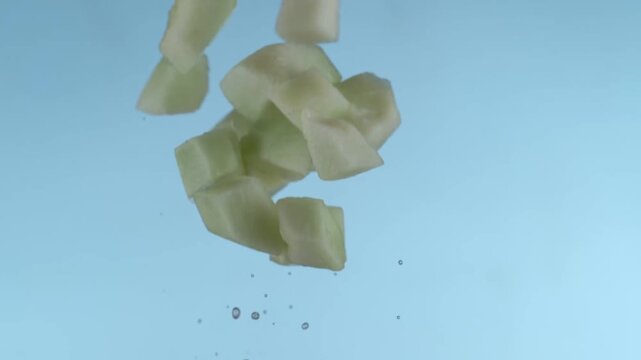Green Melon Cubes Falling Downward Against A Light Blue Background