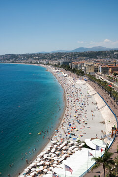 Panoramic view of the sun-drenched Nice coastline, showing the vast pebble beach and the curve of the Mediterranean shore