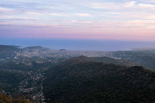 A panoramic view of Nice and the Mediterranean Sea from the mountains under a soft pink and purple twilight sky