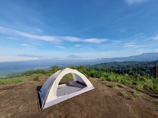 Small camping tent pitched on top of a mountain hill overlooking foggy valley and distant peaks under clear blue sky © Danang