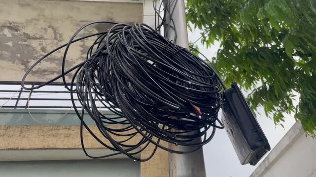 Large Coil of Black Electrical Cables Mounted on Outdoor Building iron pole