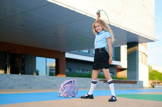 Happy schoolgirl jumping rope outdoors near school building