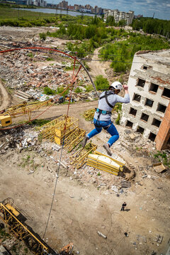 Woman in helmet rope jumping with arms spread near abandoned building and construction crane parts, extreme sport adrenaline and thrill concept