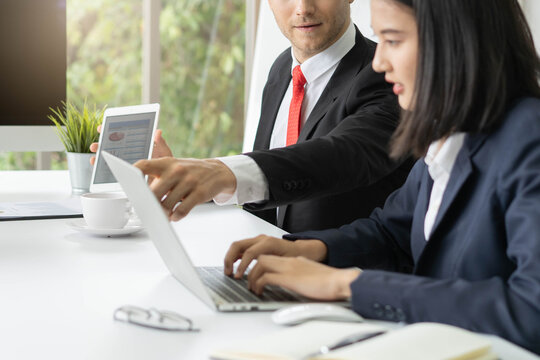 Corporate business people working together in modern office, male manager pointing at laptop screen mentoring young female employee during data analysis and presentation