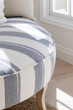 Closeup of navy-striped linen upholstery on a curved bench in a modern coastal dressing room with soft morning light illuminating the fabric