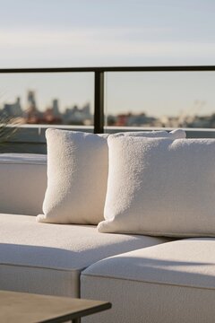 Closeup of cream boucl cushions on urban rooftop sectional with blurred skyline and warm afternoon light enhancing the texture