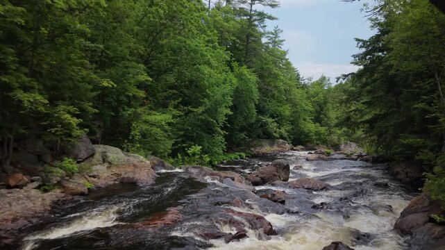 Low-altitude forward drone fly along the rushing Smith River beneath the Route 3A arch bridge surrounded by green forest, Bristol, New Hampshire, USA
