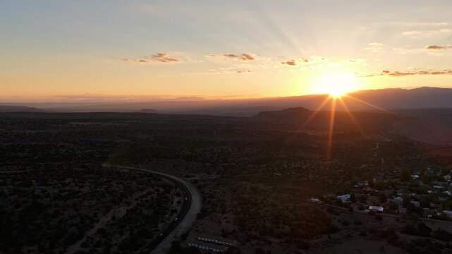 4K drone timelapse of early morning commuter traffic winding along a highway in White Rock, New Mexico. The bright sun rises over the distant Sangre de Cristo mountains, illuminating the sky.