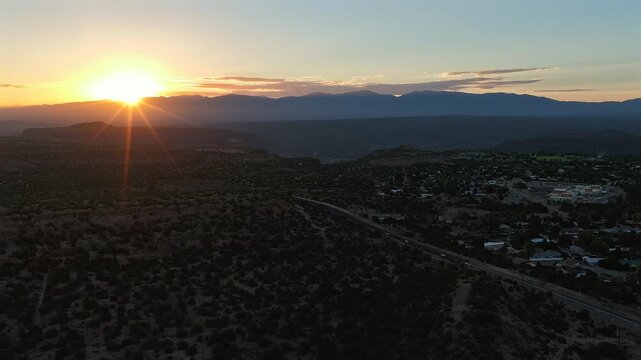 4K drone hyperlapse of a golden sunrise over the chaparral landscape of White Rock, New Mexico. A bright sunstar crests the distant Sangre de Cristo mountains beside the main road into town.